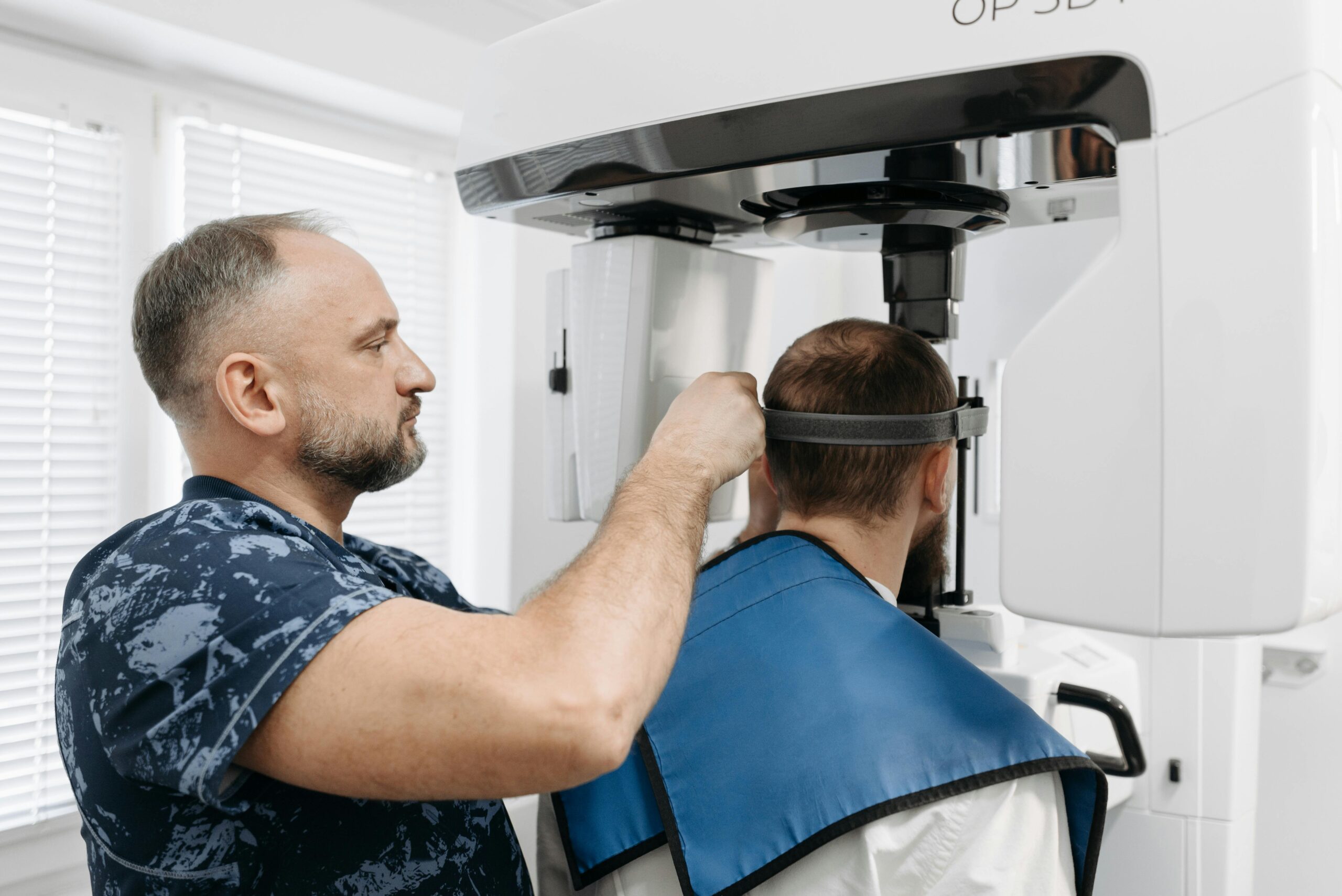 A technician adjusts a headband on a patient seated for a dental scan using a large imaging machine in a bright, clinical room. If you have dental questions or are choosing a dentist in TX, such technology shows commitment to advanced care.