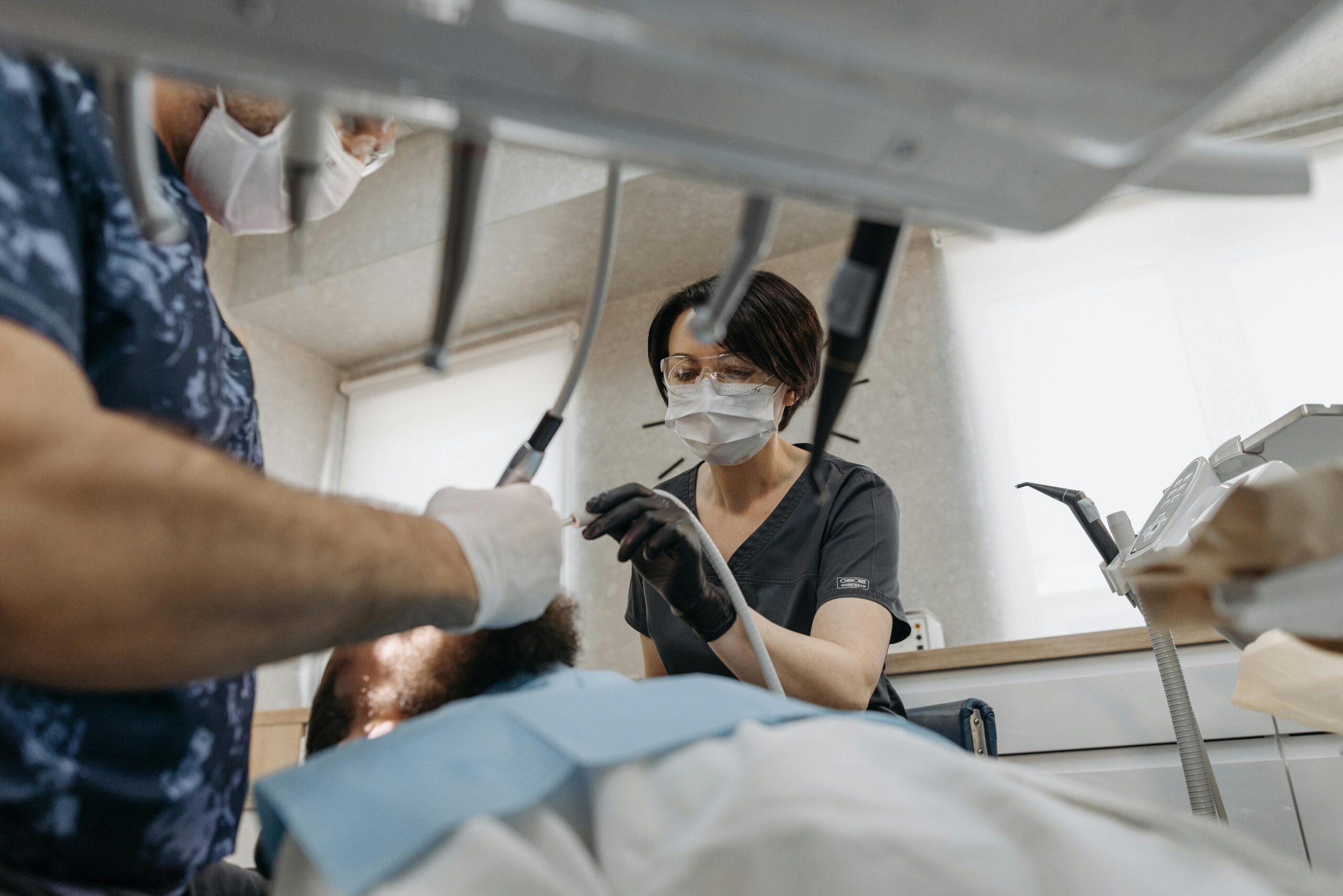 A dentist in Irving TX and an assistant, both wearing masks and gloves, perform a dental procedure on a patient lying in a dental chair—a helpful scene for anyone choosing a dentist or preparing questions to ask their dentist.